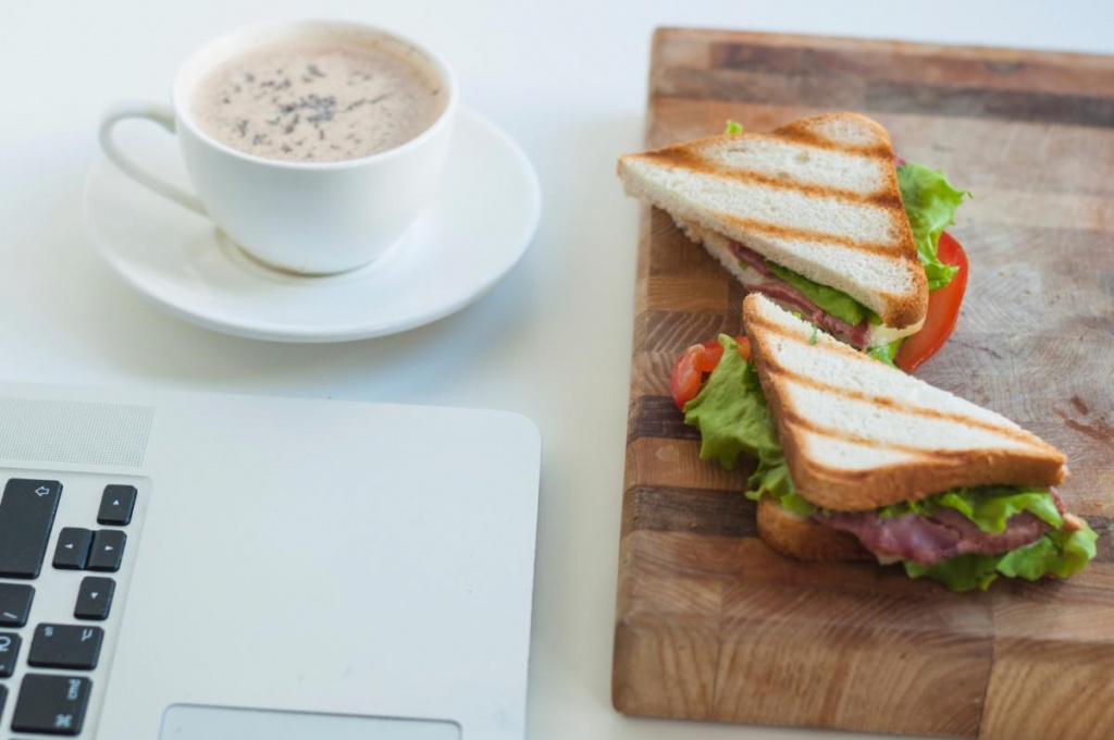 close-up-laptop-coffee-cup-sandwiches-chopping-board-against-white-background.jpg